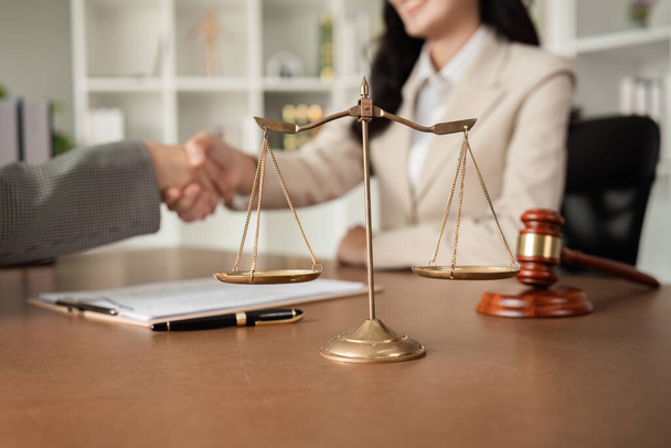 Een advocaat en een zakenvrouw schudden elkaar de hand en bereiken overeenstemming over een samenwerkingscontract. In het advocatenkantoor ligt er een hamer op tafel... - Foto, afbeelding