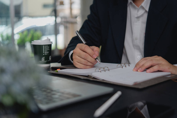 Un uomo d'affari lavora pianificando o scrivendo appunti in un quaderno, con un portatile e una tazza di caffè sul tavolo.. - Foto, immagini