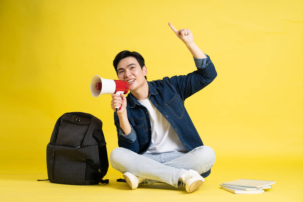 Portret van Aziatische mannelijke student poseren op gele achtergrond - Foto, afbeelding