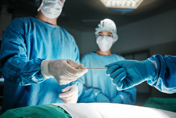 Surgeon, hands and scalpel in operating room at hospital in scrubs, ppe or emergency healthcare procedure. Doctors, group and together in icu, medical surgery or tools for help for wellness at clinic. - Photo, Image