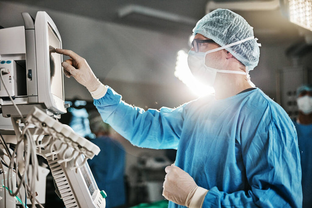 Surgery, machine and doctor with monitor in theatre for healthcare, cardiovascular operation or analysis. Medical professional, man and scrubs with equipment for cardiology, procedure or information. - Photo, Image