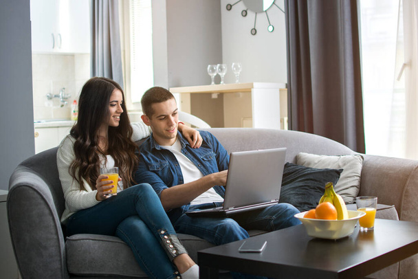 Gyönyörű fiatal pár használja laptop, miközben ül a kanapén együtt otthon - Fotó, kép