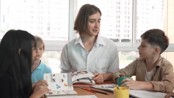 Professional caucasian teacher telling story to diverse student while sitting at table with storybook and colored book. Smart learner listening story while colored picture from instructor. Erudition. - Footage, Video