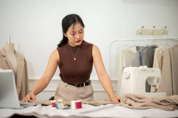 アジアのプロフェッショナルな女性ファッションデザイナーまたはテーラーは,アトリエスタジオでの彼女の仕事に焦点を当て,服のパターンをチェックして調整しています. - 写真・画像