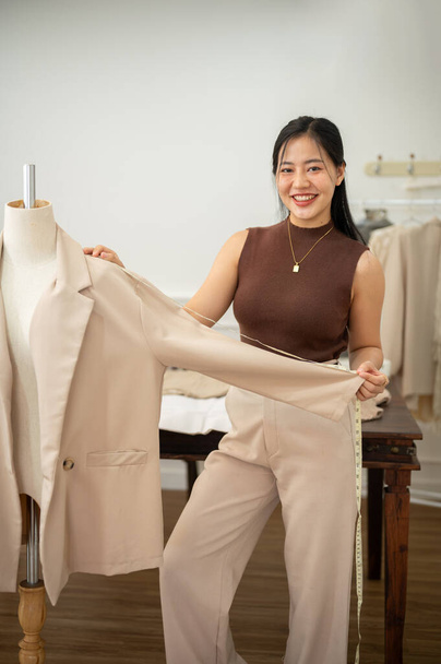 Una atractiva diseñadora de moda asiática o sastre está trabajando en su estudio, revisando el patrón de su traje en un maniquí de sastre. modista, costurera, fabricante de trajes - Foto, Imagen