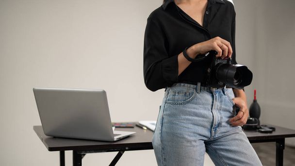Przycięte ujęcie pewnej siebie, profesjonalnej fotografki w czarnej koszuli stoi w studiu zdjęciowym z lustrzanką w ręku. - Zdjęcie, obraz