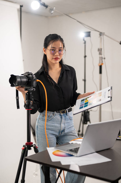 Een coole, aantrekkelijke Aziatische fotografieproducent werkt in een fotostudio en bekijkt beelden op haar laptop. - Foto, afbeelding