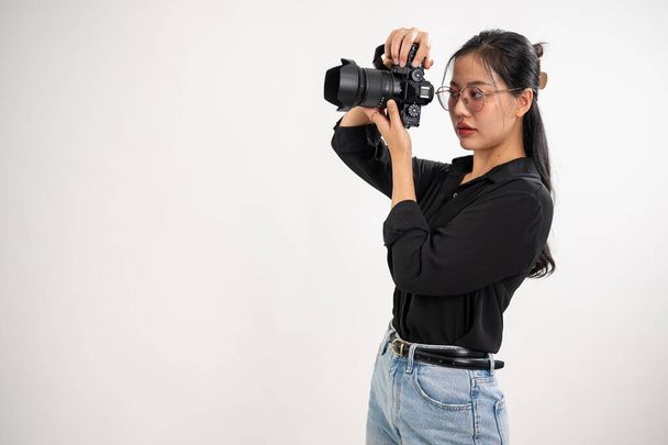 Profesjonalna, pewna siebie azjatycka fotografka w czarnej koszuli robi zdjęcia w studiu sesyjnym, trzymając profesjonalną lustrzankę blisko twarzy. - Zdjęcie, obraz