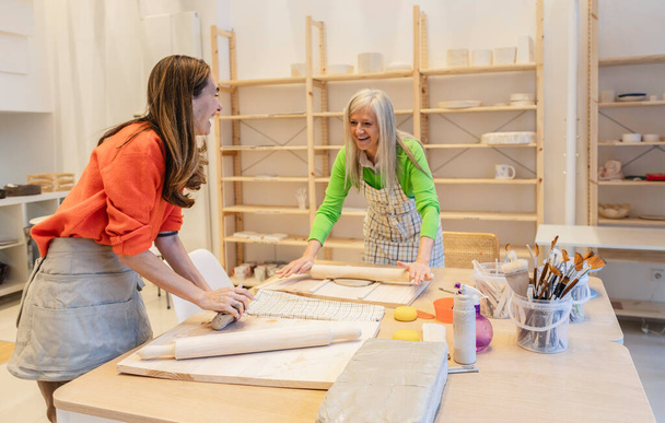 Une femme âgée et sa fille adulte profitent d'un moment de création dans un studio de poterie ensoleillé. - Photo, image
