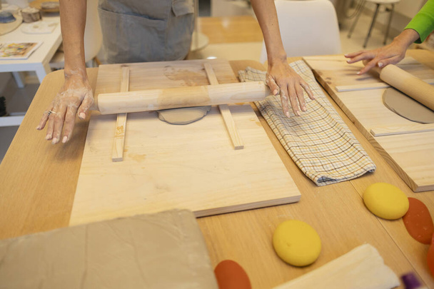 Uma visão detalhada de mãos hábeis rolando argila, com ferramentas de cerâmica no pronto em uma oficina. - Foto, Imagem
