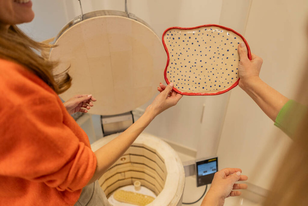 Dos artesanos exhiben una placa de cerámica pintada a mano con lunares antes de cocer el horno. - Foto, imagen