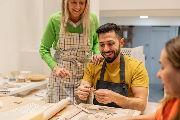 Una instructora senior y un estudiante masculino comparten un momento alegre en una clase de cerámica. - Foto, imagen