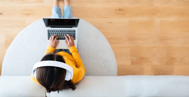 Top weergave van jonge Aziatische vrouw zitten op de vloer en werken op computer laptop, het dragen van draadloze headset, luisteren naar muziek - Foto, afbeelding