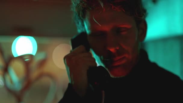 Un uomo sta parlando al telefono in stile noir in cabina in neon ligth. L'immagine ha un'atmosfera scura e lunatica, con il volto dell'uomo illuminato dalla luce dei telefoni - Filmati, video