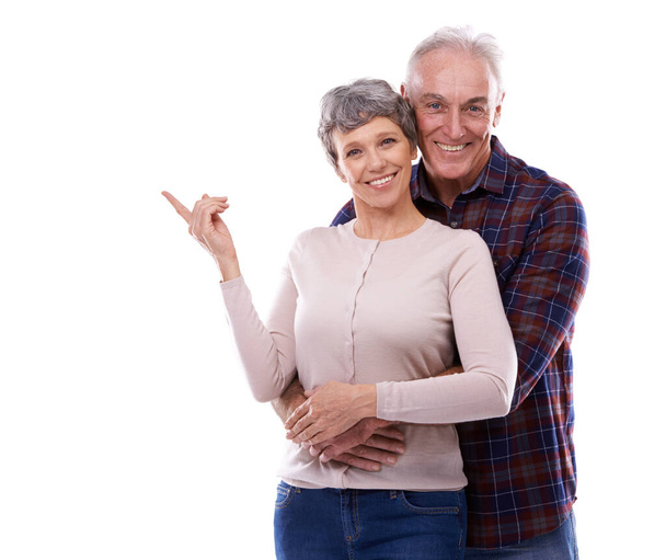 Happy, pointing and senior couple in studio, hug together or customer loving relationship for retired people. Information, advertising or presentation on background, promotion show on mockup space. - Photo, Image