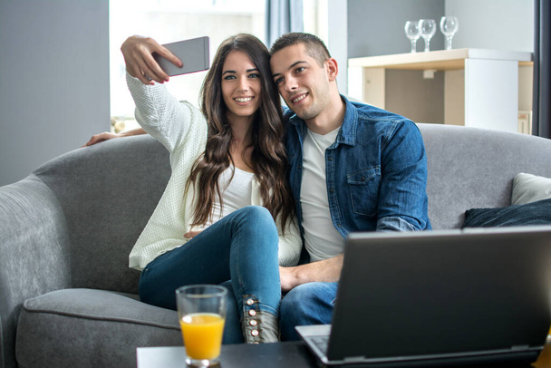 Giovane coppia sorridente che si fa un selfie con smartphone a casa - Foto, immagini
