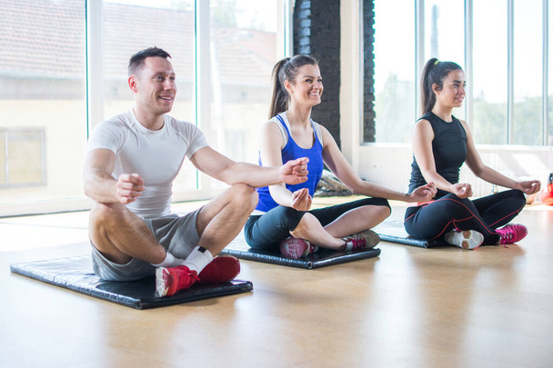 Groupe de jeunes amis sportifs pratiquant le yoga, assis jambes croisées sur le sol en position lotus à la salle de gym - Photo, image