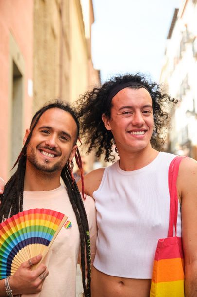 Schwules Paar lächelt, blickt in die Kamera und hält einen Regenbogenfan während des Internationalen Pride Day. - Foto, Bild