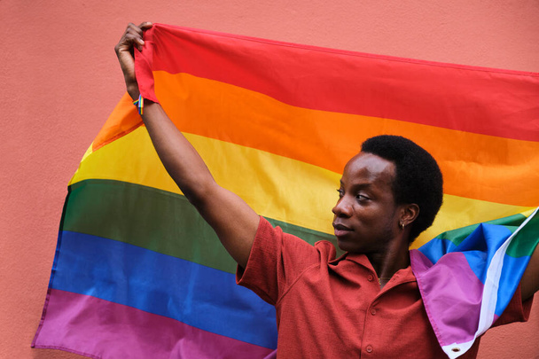 Γκέι μαύρος άνδρας με σημαία ουράνιου τόξου που αντιπροσωπεύει την ποικιλομορφία και την ένταξη της ΛΟΑΤΚΙ κοινότητας. - Φωτογραφία, εικόνα