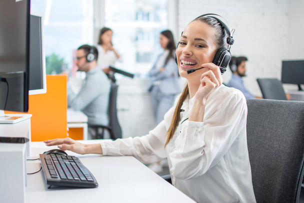 Beautiful female call center consultant with headphones working in office. - Photo, Image