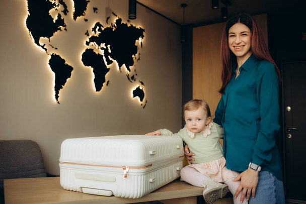 une jeune mère avec une fille avec une valise dans une agence de voyages - Photo, image