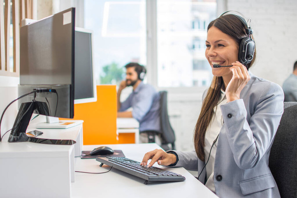 Portrait of happy smiling female customer support phone operator at workplace. - Photo, Image