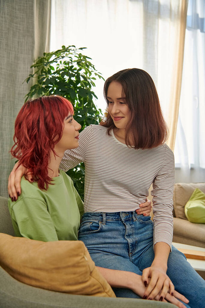 gelukkig lesbisch vrouw in haar twintiger jaren zitten op ronden van haar vriendin terwijl het doorbrengen van tijd in woonkamer - Foto, afbeelding