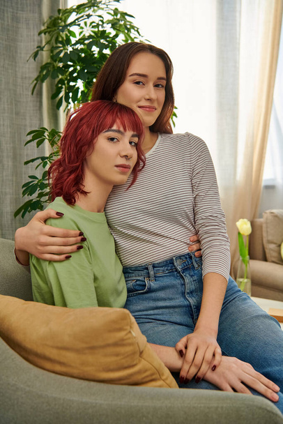 gelukkig lesbisch vrouw in 20s zitten op ronden van haar vriendin terwijl rusten samen in woonkamer - Foto, afbeelding
