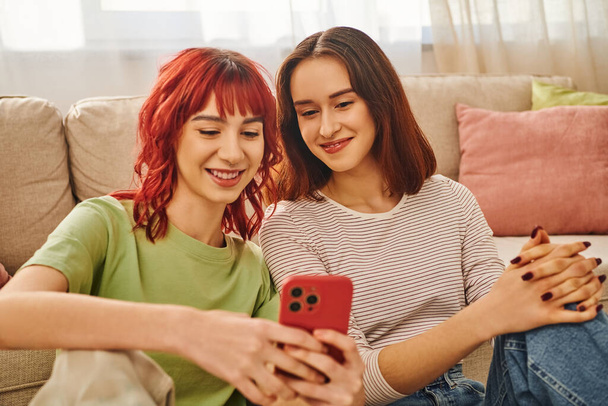 young lesbian couple smiling and using smartphone together, modern lifestyle and connection - Фото, изображение