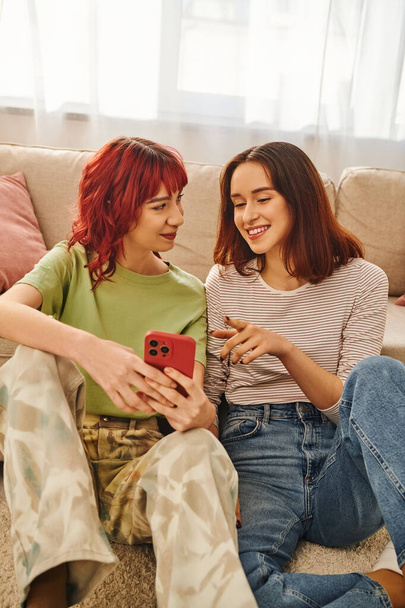 happy young lesbian couple smiling and using smartphone together, modern lifestyle and connection - Zdjęcie, obraz