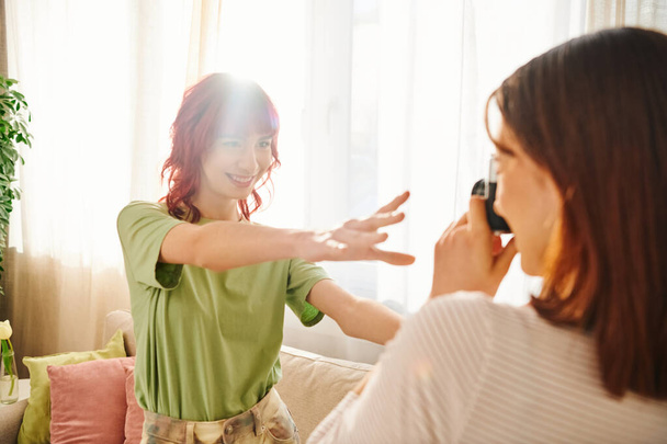 Playful photo session at home of young lesbian woman capturing her girlfriend cheerful pose - Photo, Image
