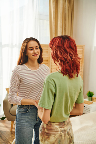 feliz joven lesbiana de la mano con su novia en apartamento moderno, cariñoso - Foto, imagen