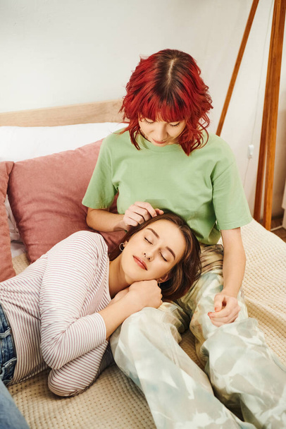 Νεαρό ζευγάρι λεσβιών μοιράζονται μια τρυφερή στιγμή, γυναίκα ξαπλωμένη στην αγκαλιά της κοπέλας της στην κρεβατοκάμαρα - Φωτογραφία, εικόνα