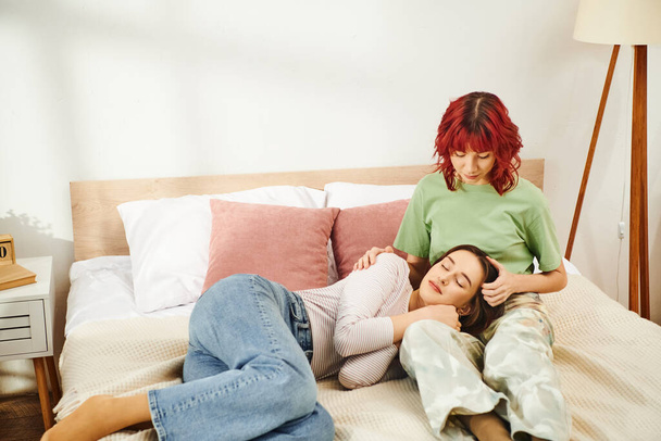Młoda lesbijka para dzieląca się piękną chwilą, kobieta leżąca na kolanach na swojej dziewczynie w sypialni - Zdjęcie, obraz