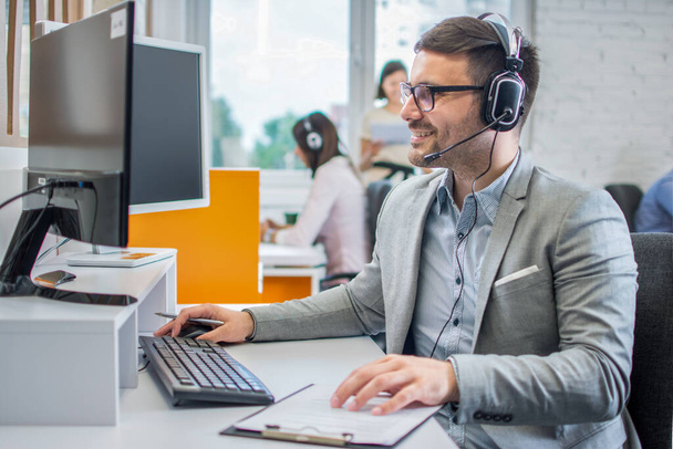 Uśmiechnięty pracownik obsługi klienta z słuchawkami pracującymi w call center. - Zdjęcie, obraz