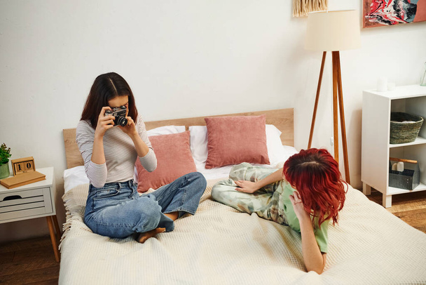 dom sesja zdjęciowa lesbijka robi zdjęcia na retro aparat jej dziewczyna na łóżku - Zdjęcie, obraz
