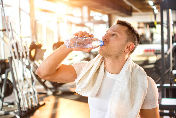 Портрет молодого красивого мужчины, пьющего воду в спортзале - Фото, изображение