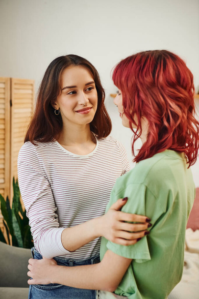 retrato de jovem e feliz mulher lésbica olhando e abraçando seu parceiro feminino com cabelo vermelho - Foto, Imagem