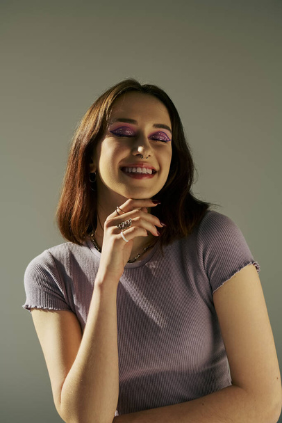 bold makeup of happy young girl in 20s posing in t-shirt with closed eyes and purple eye shadow - Fotoğraf, Görsel