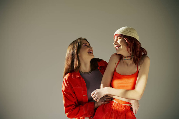 happy lgbt couple in vibrant attire standing together and holding hands on grey backdrop, laughter - Foto, imagen