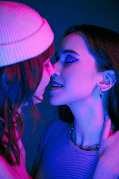 Intieme kus onder paarse lichten van stijlvolle lesbische paar met gedurfde make-up, generatie z liefde - Foto, afbeelding