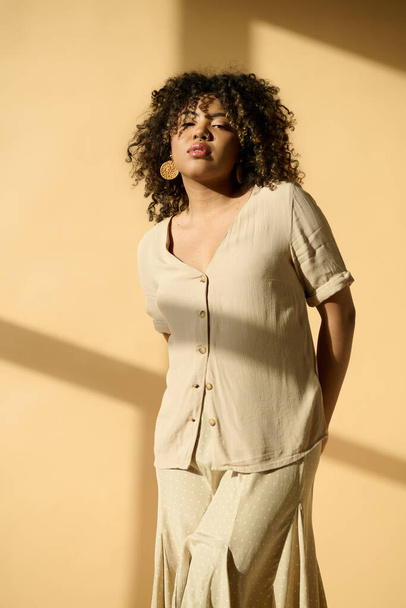 Eine schöne junge Afroamerikanerin mit lockigem Haar steht anmutig vor einer lebhaften gelben Wand. - Foto, Bild