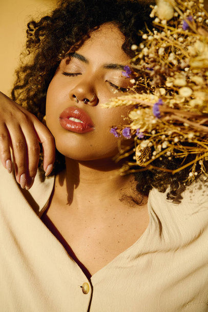 Uma bela mulher afro-americana com cabelo encaracolado segurando um bando vibrante de flores em um ambiente de estúdio. - Foto, Imagem