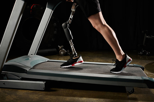 Uma pessoa com uma perna protética trabalha em uma esteira, com uma máquina visível no fundo. - Foto, Imagem