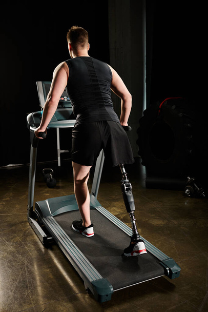 Un hombre con una pierna protésica está caminando en una cinta de correr en una habitación con poca luz, centrándose en su rutina de entrenamiento. - Foto, imagen