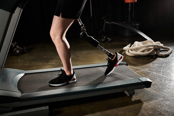 Una persona con una gamba protesica cammina su un tapis roulant in palestra, mostrando determinazione e forza nella loro routine di allenamento.. - Foto, immagini