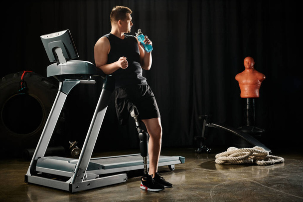 A man with a prosthetic leg stands on a treadmill, holding a bottle of water. - Photo, Image
