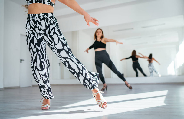 Graceful dancing women group doing elegant dance movements in white color spacious hall with big mirror wall.People's expressions during dancing, beauty of woman's body, active lifestyle concept image - Foto, imagen