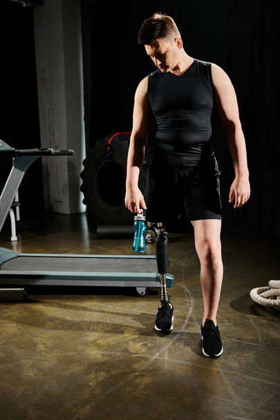 Un uomo con una gamba protesica si trova accanto a una macchina, concentrandosi sulla sua routine di allenamento in palestra.. - Foto, immagini