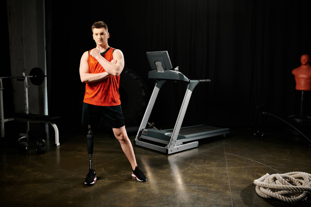 Um homem com uma perna protética fica na frente de uma esteira, pronto para começar sua rotina de exercícios no ginásio. - Foto, Imagem